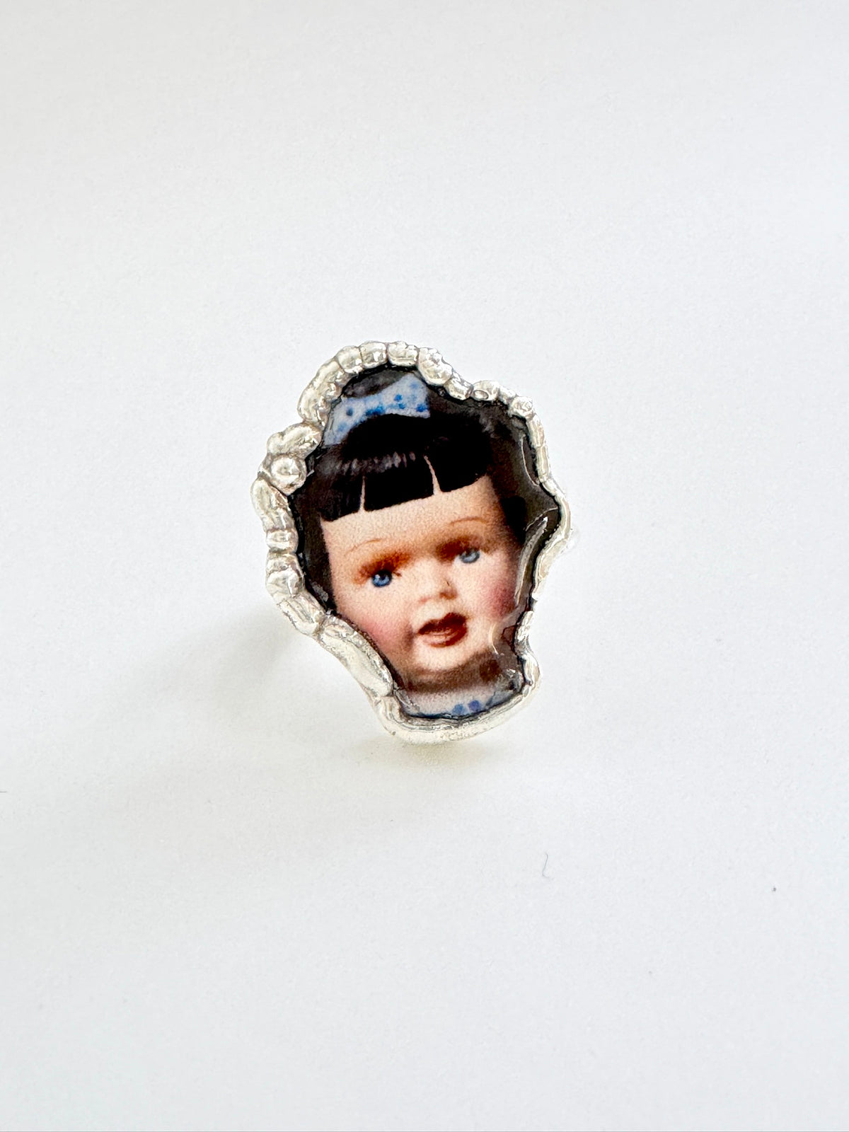 Blue bow doll head statement ring in fine silver, size 9, from FOXLARK’s The Weirdlings Collection, featuring intricate detailing.