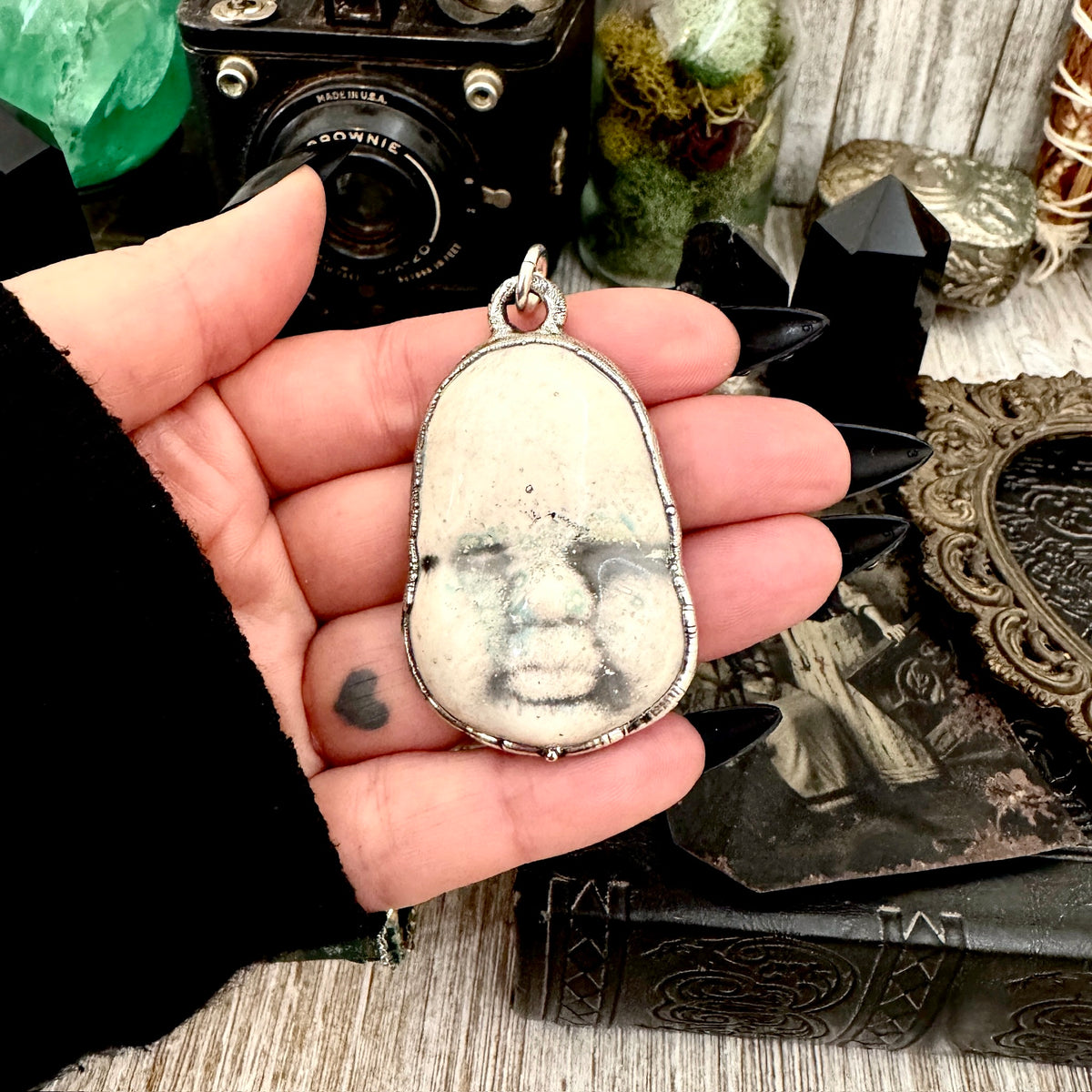 Close-up of FOXLARK ceramic baby doll face necklace in fine silver, showcasing detailed craftsmanship and unique design.