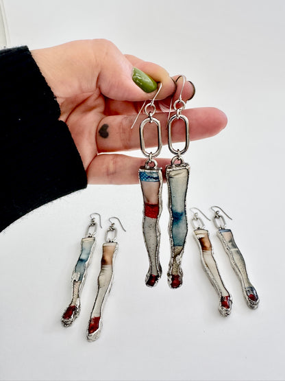 Long mismatched silver doll leg earrings from FOXLARK's Weirdlings Collection, featuring unique dangling, statement jewelry.